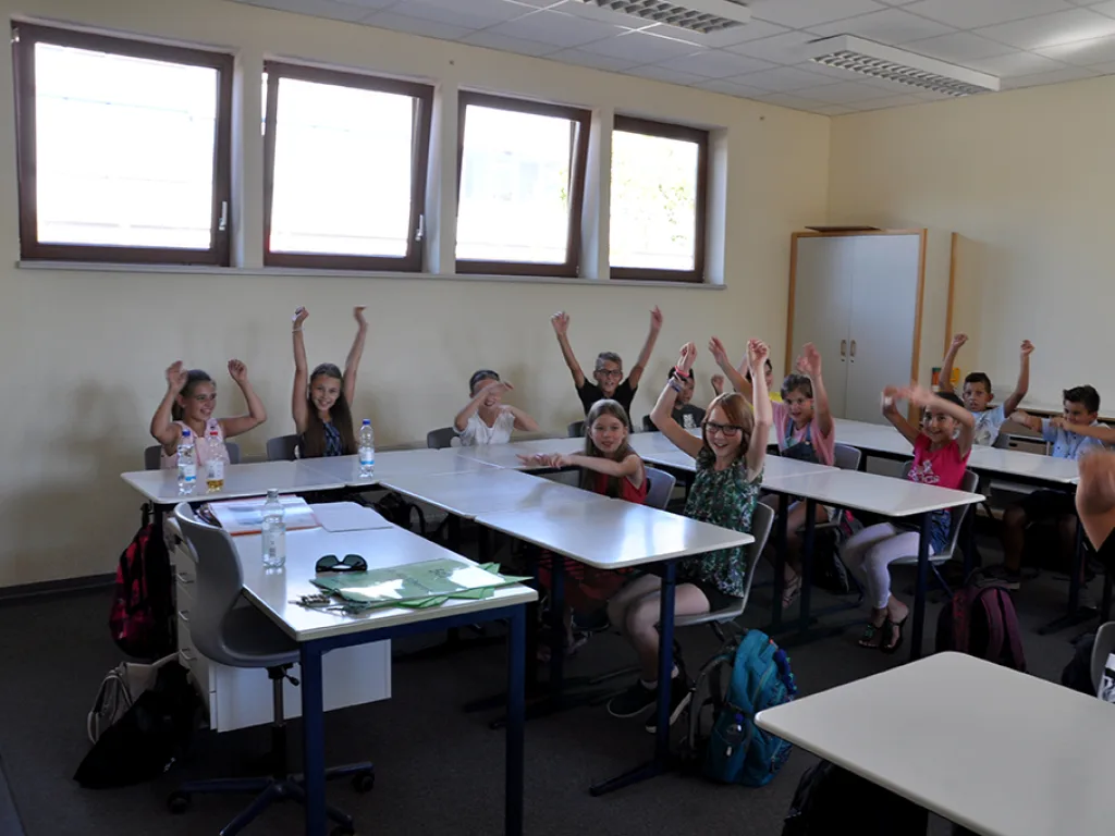 Kinder melden sich in einem hellen Klassenraum.